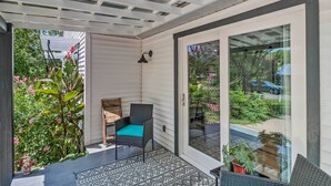 A covered patio area with a chair and a table, a glass door leading outside, and a view of greenery and a car in the distance. - Mountain View Home Steps to Amphitheater Park (Mountain View)