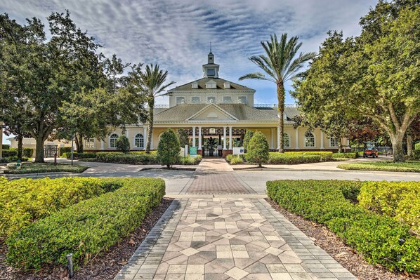 A building with a central entrance, surrounded by well-maintained hedges and palm trees. - Relax & Play: Townhome Near Disney & More! (Reunion)