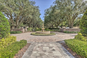 A paved garden with a central fountain, surrounded by trimmed hedges and trees. - Relax & Play: Townhome Near Disney & More! (Reunion)