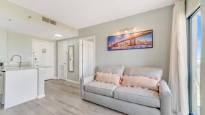 Ein modernes Wohnzimmer mit grauem Sofa, einer Küchenzeile und einem Stadtbild an der Wand.
