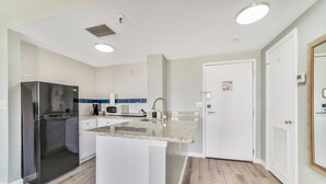 Eine moderne Küche mit einem Edelstahlkühlschrank, einer zentralen Kochinsel mit Spüle und weißen Schränken.