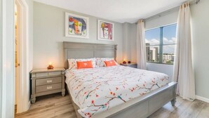 Ein Schlafzimmer mit einem großen Bett, zwei Nachttischen, einem Fenster mit Vorhängen und einem Bild an der Wand.