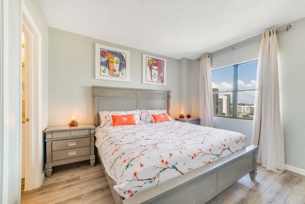 A bedroom with a large bed, two nightstands, a window with curtains, and artwork on the wall. - Fabulous Resort Condo with Heated Pool! (Orange County)