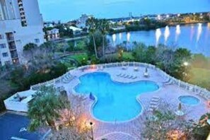 A swimming pool with a unique design, surrounded by a landscaped area with trees and a view of a body of water. - Fabulous Resort Condo with Heated Pool! (Orange County)