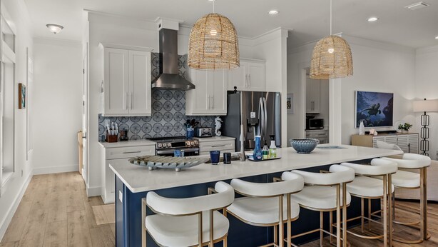 A modern kitchen with white cabinets, a large island with bar stools, and a hanging woven light fixture. - New!!  The Blue Pelican!  Stunningl canal front beauty with direct gulf access! (Sanibel)