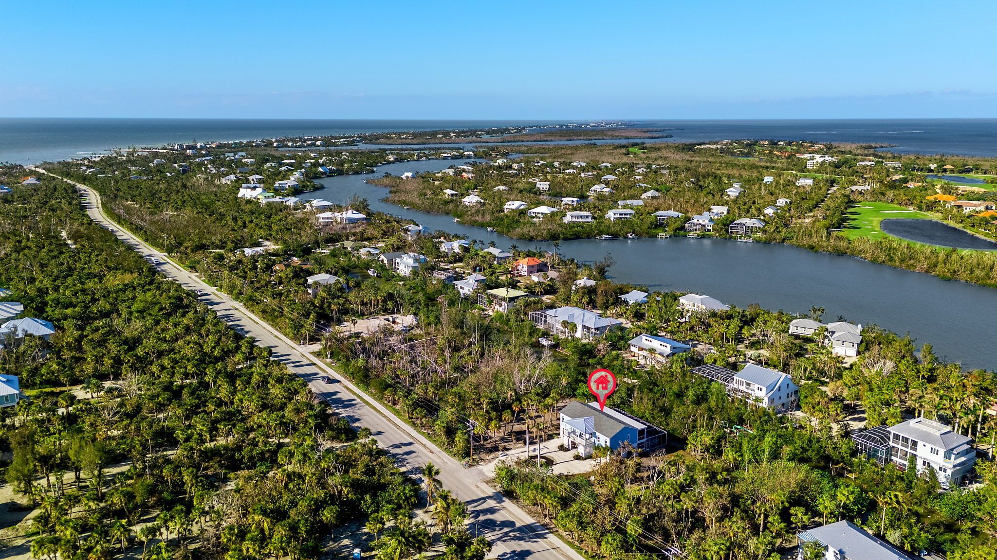 An aerial view of a coastal residential area with houses, a road, and a golf course.