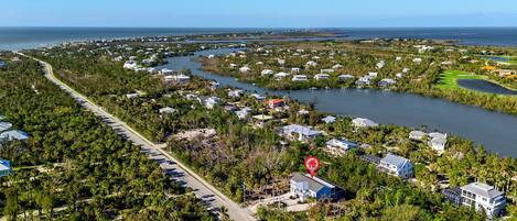 An aerial view of a coastal residential area with houses, a road, and a golf course.