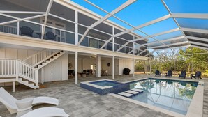A modern outdoor pool area with a glass-enclosed deck, lounge chairs, and a hot tub. - New!!  The Blue Pelican!  Stunningl canal front beauty with direct gulf access! (Sanibel)