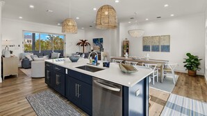 A modern kitchen with a central island, white cabinetry, and a dining area with a wooden table and chairs. - New!!  The Blue Pelican!  Stunningl canal front beauty with direct gulf access! (Sanibel)