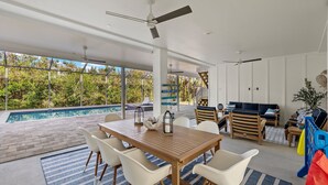 A modern outdoor living area with a pool, wooden furniture, and ceiling fans. - New!!  The Blue Pelican!  Stunningl canal front beauty with direct gulf access! (Sanibel)