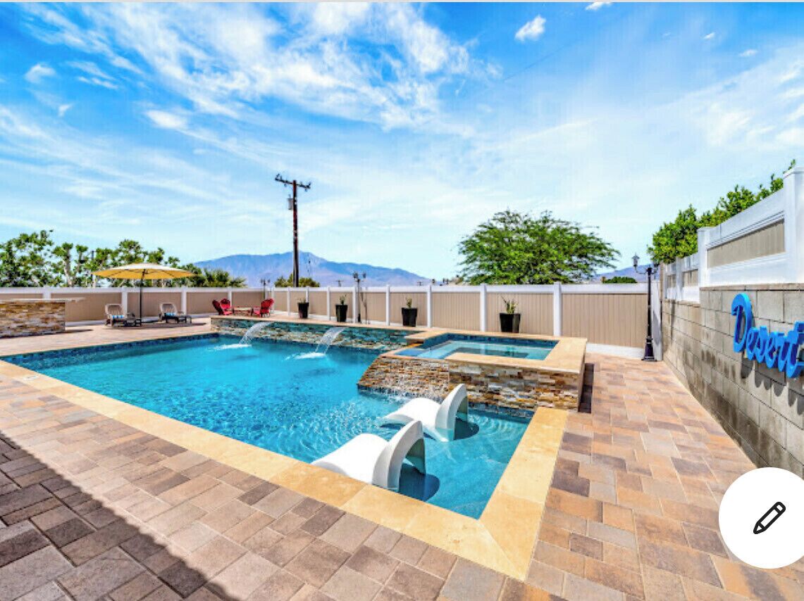 A swimming pool with a stone border, lounge chairs, and a view of mountains.