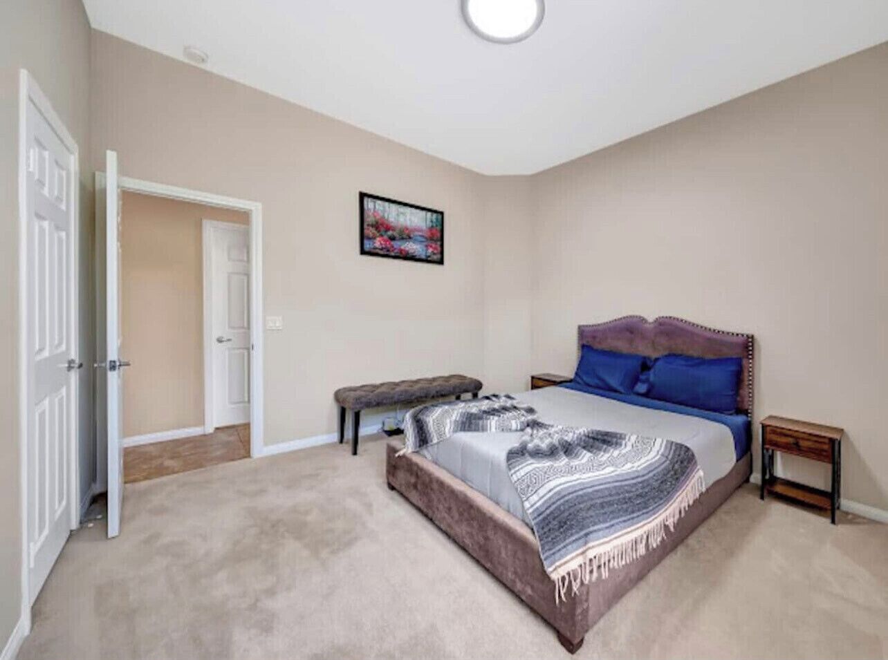 Un dormitorio con una cama grande, un banco, una puerta y un cuadro en la pared.