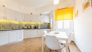 Una cocina moderna con armarios blancos, piso de madera y un comedor con mesa y sillas blancas.