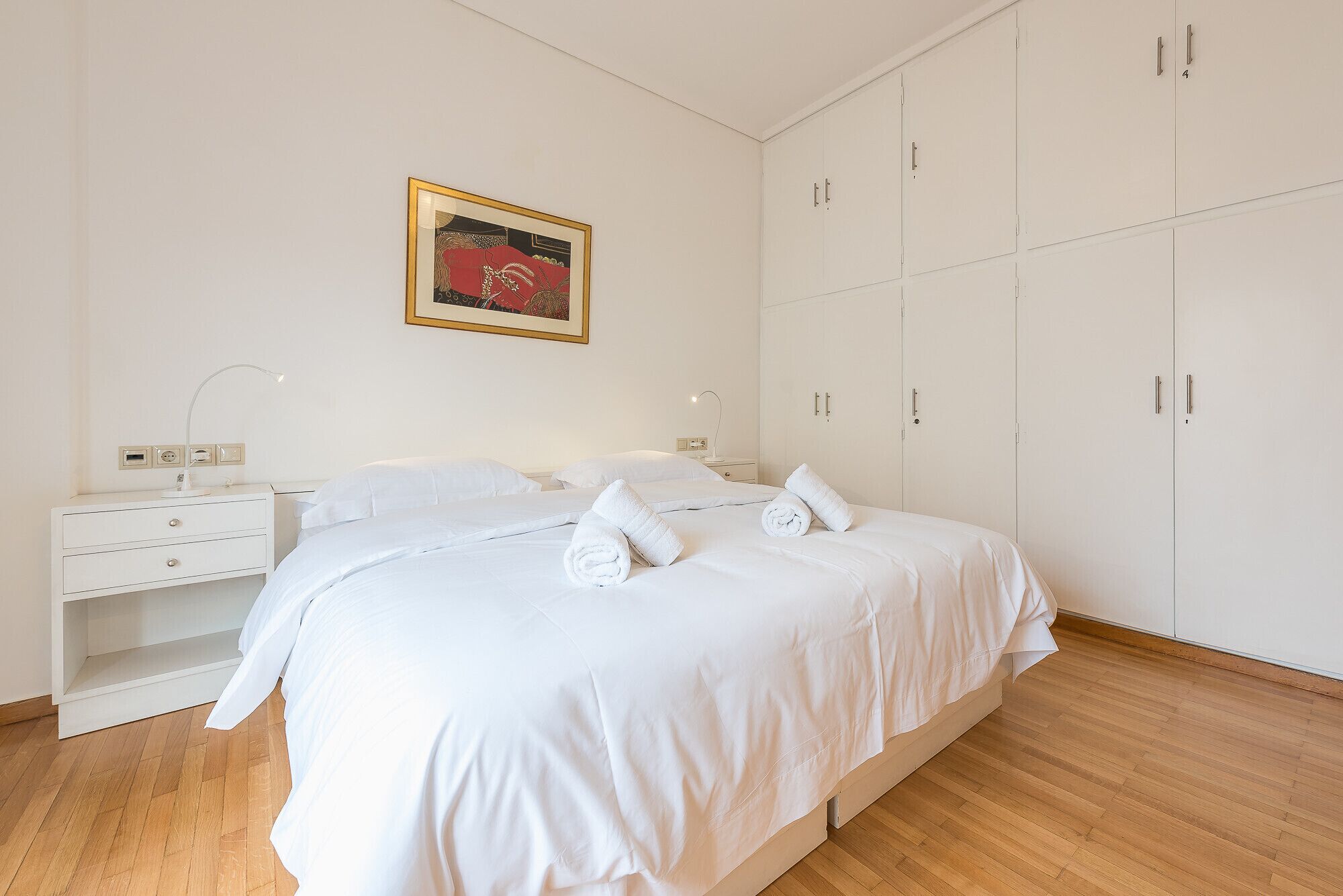 A neatly arranged bedroom with a bed, bedside tables, a wardrobe, and a framed picture on the wall.