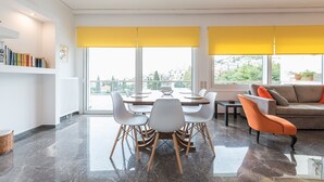 Una sala de estar moderna con comedor, ventanas grandes con persianas amarillas, un sofá y una estantería.