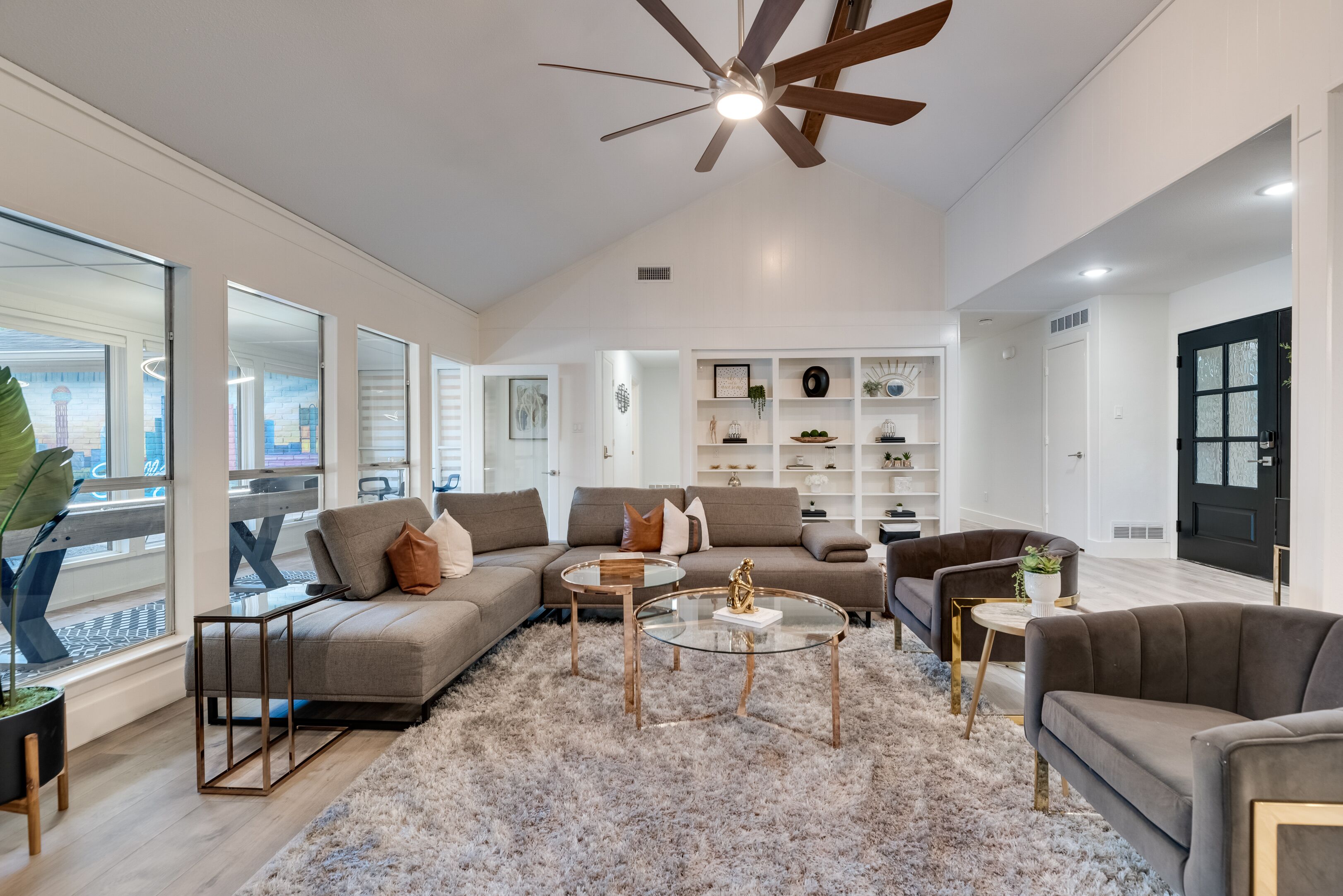 A modern living room with a sectional sofa, a glass coffee table, and a ceiling fan.