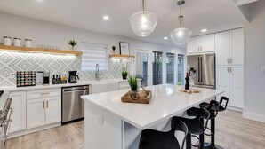 A modern kitchen with white cabinetry, stainless steel appliances, and a central island with bar stools. - Lux Dallas Oasis- Pool, Hot Tub, Firepit, Game Room, Sleeps 12 (Dallas)