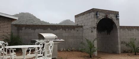 An outdoor patio with a barbecue grill, white ornate chairs, and a stone archway.