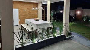 An outdoor dining area with a table and chairs, a refrigerator, and potted plants.