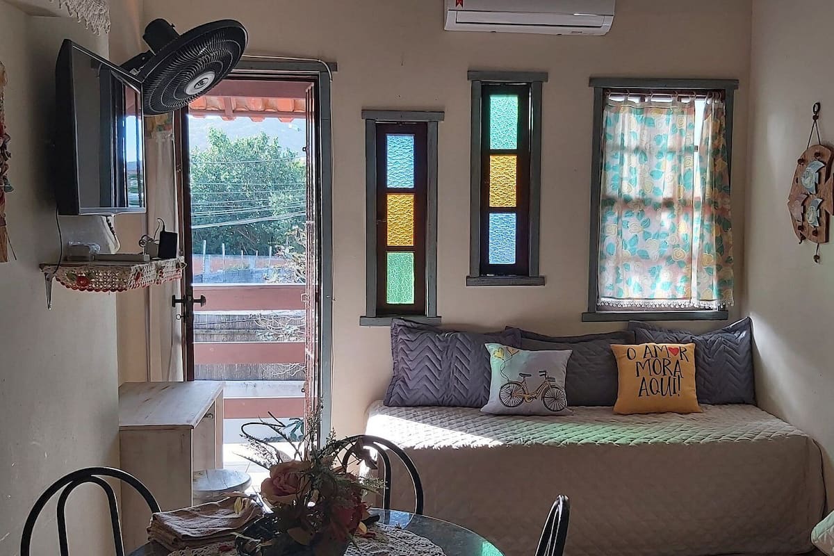 Um quarto aconchegante com uma cama, uma mesa com um vaso e uma janela com cortinas estampadas.