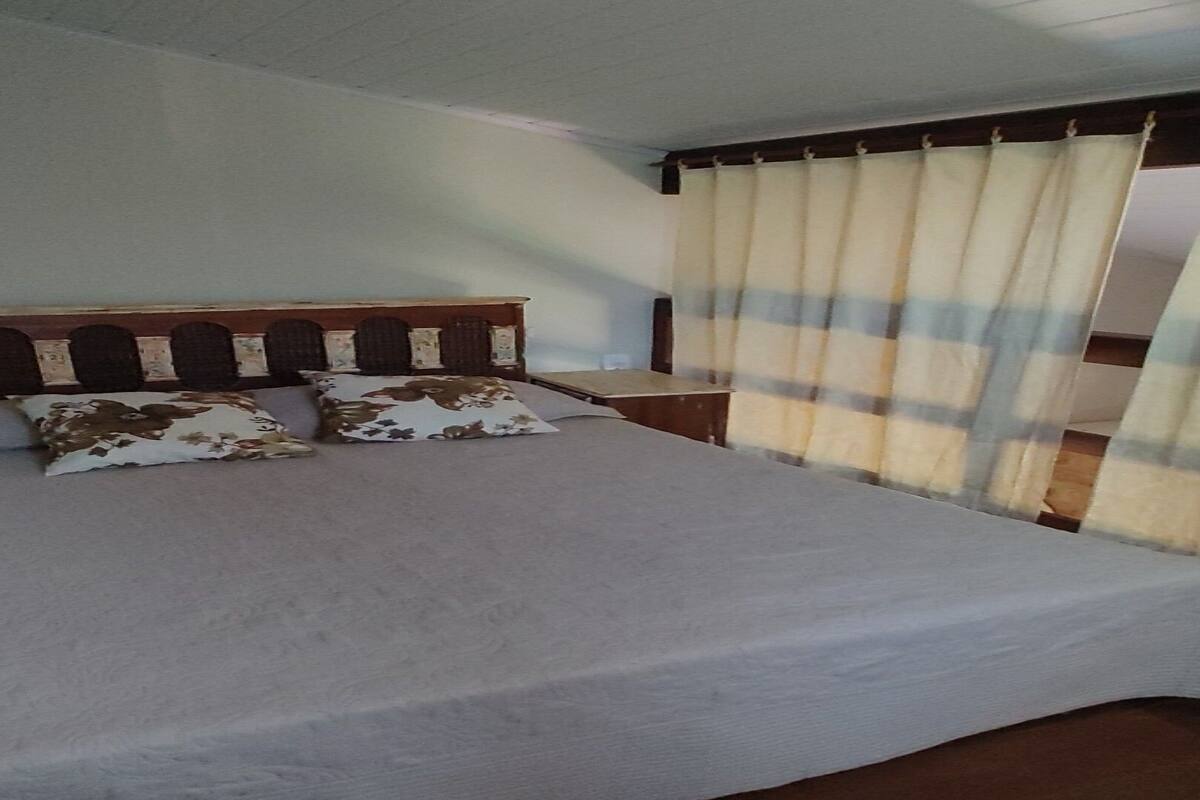 Cama com cabeceira de madeira, duas almofadas e cortina listrada.