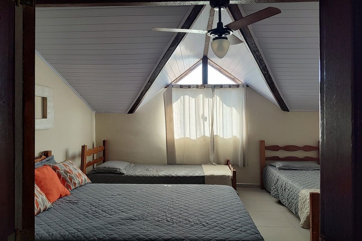 Quarto com duas camas, um ventilador de teto e janela com cortinas.