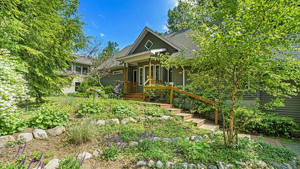 A house with a front porch, a wooden staircase, and a garden with various plants and rocks.