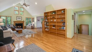 A spacious living room with a fireplace, wooden bookshelves, and a high ceiling with a fan.