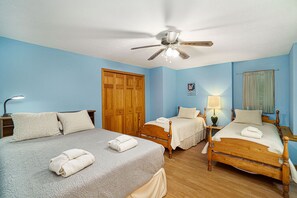 Classic hotel room with two single beds and a large bed, featuring a wooden wardrobe and ceiling fan.