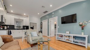 A modern living room with a glass coffee table, a sofa, a TV mounted on the wall, and a bookshelf. - Downtown Dunedin Cozy 1 bedroom Cottage (Dunedin)