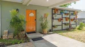 A house with a front door labeled 'COOL COTTAGE,' a small porch, and a wall-mounted planter with various plants. - Downtown Dunedin Cozy 1 bedroom Cottage (Dunedin)