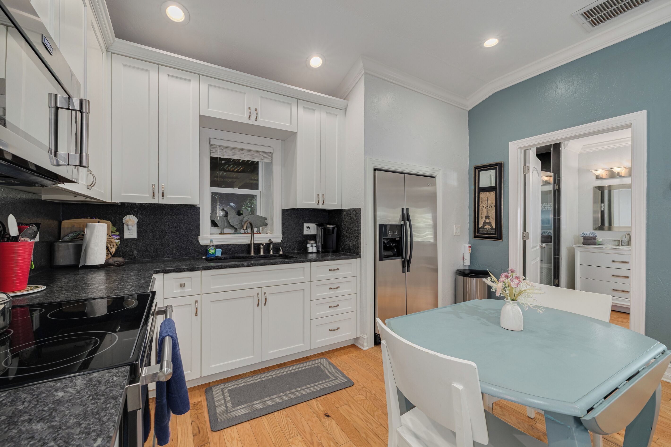 A modern kitchen with white cabinets, a black countertop, stainless steel appliances, and a blue dining table.