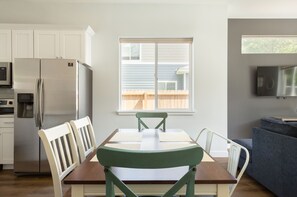 A modern kitchen with white cabinets, a stainless steel refrigerator, and a dining table with chairs.