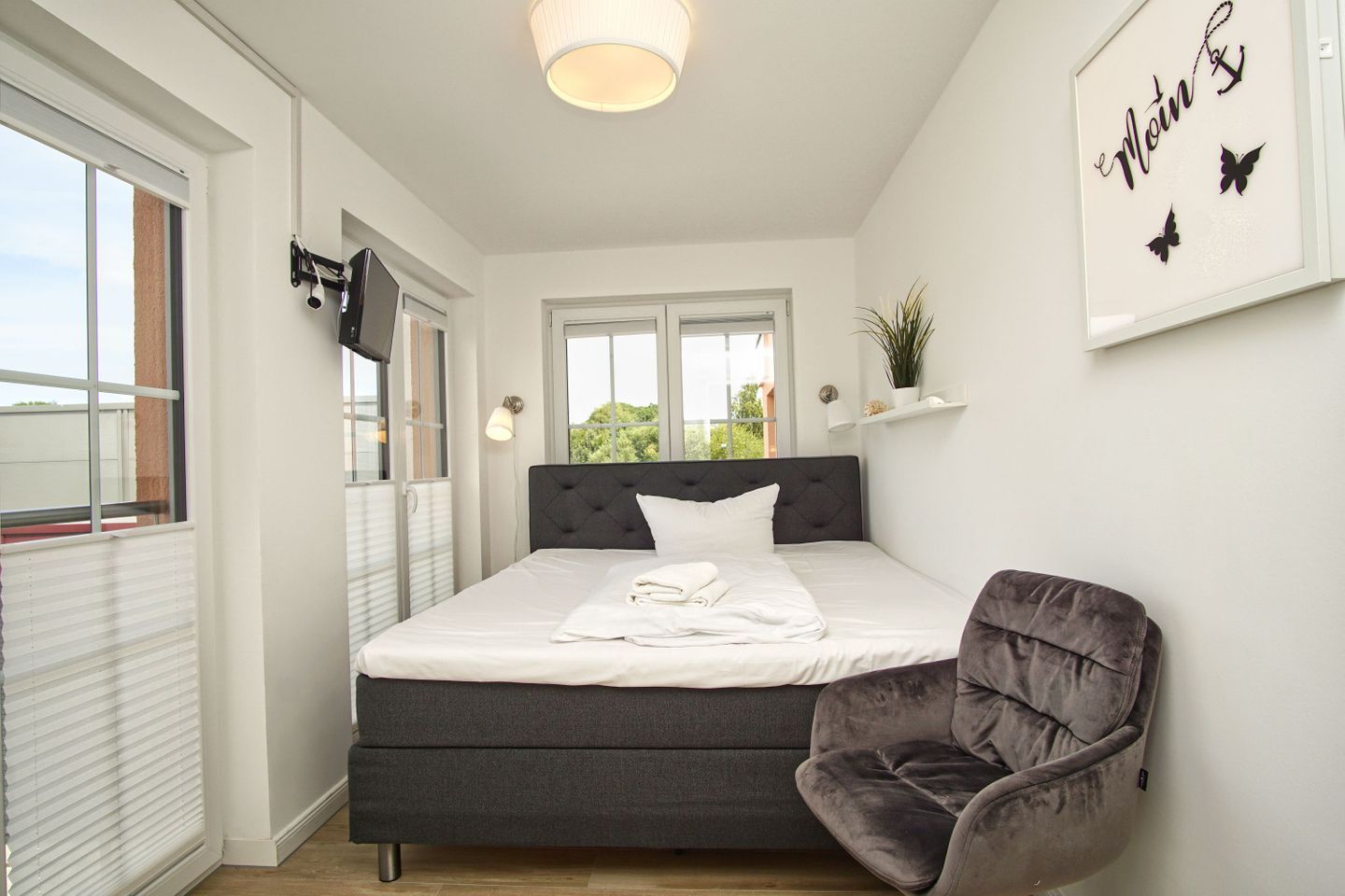 A bedroom with a bed, a chair, a window, and a wall with a sign.