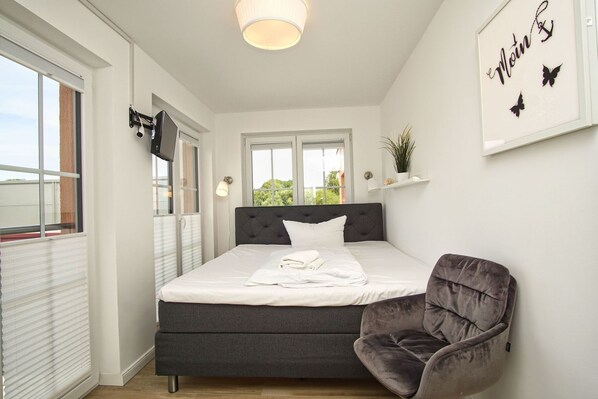 A bedroom with a bed, a chair, a window, and a wall with a sign.