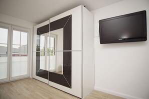Ein Zimmer mit einer Schiebeglasdoor, einem an der Wand befestigten Flachbildfernseher und einem Holzboden.