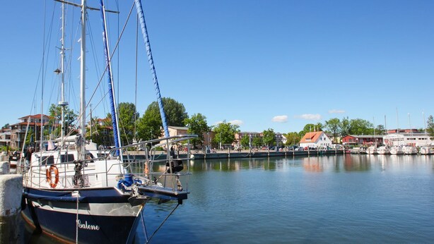Ein Hafen mit vertäuten Booten, einem klaren Himmel und Gebäuden im Hintergrund.