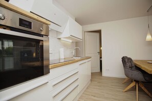 A modern kitchen with white cabinetry, a black oven, a wooden countertop, and a grey chair.