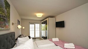 Ein Hotelzimmer mit einem großen Bett, einem Nachttisch, einer Lampe, einem Fernseher und einer Schiebetür zu einem Außenbereich.