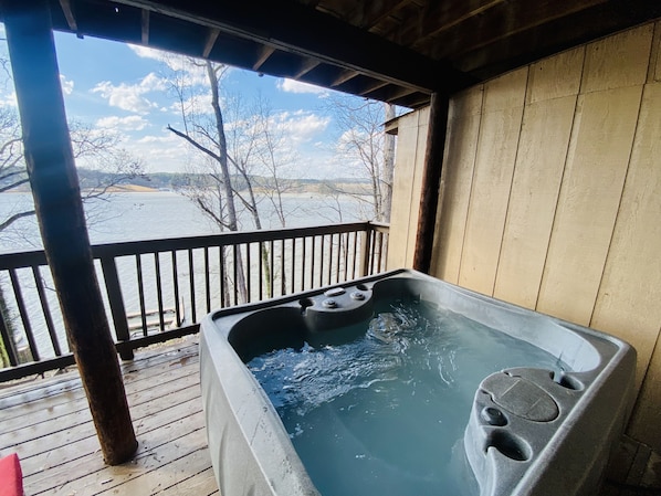 A hot tub on a wooden deck with a view of a lake and trees.