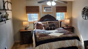 Une chambre avec un grand lit, deux tables de chevet, un ventilateur de plafond et une fenêtre avec des stores.