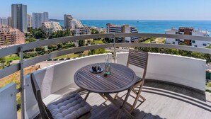 Un balcon avec une table ronde et des chaises, offrant une vue sur le paysage urbain et la mer.