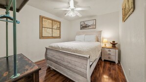 Une chambre à coucher avec un lit en bois, une table de chevet avec une lampe, un ventilateur de plafond et deux œuvres d’art accrochées au mur.