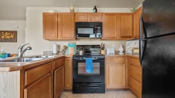 Una cocina con gabinetes de madera, una estufa negra, un microondas y un refrigerador.