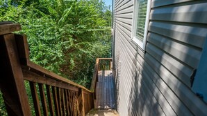 A wooden staircase leading to a house with a window, surrounded by dense green foliage.