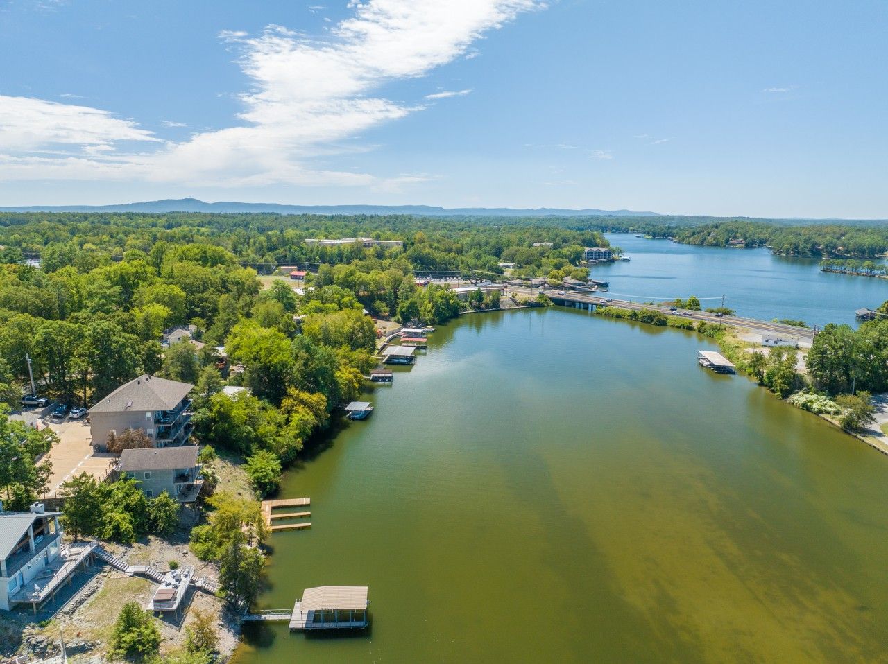 An aerial view of a riverside property with multiple buildings, docks, and a bridge connecting to a larger body of water.