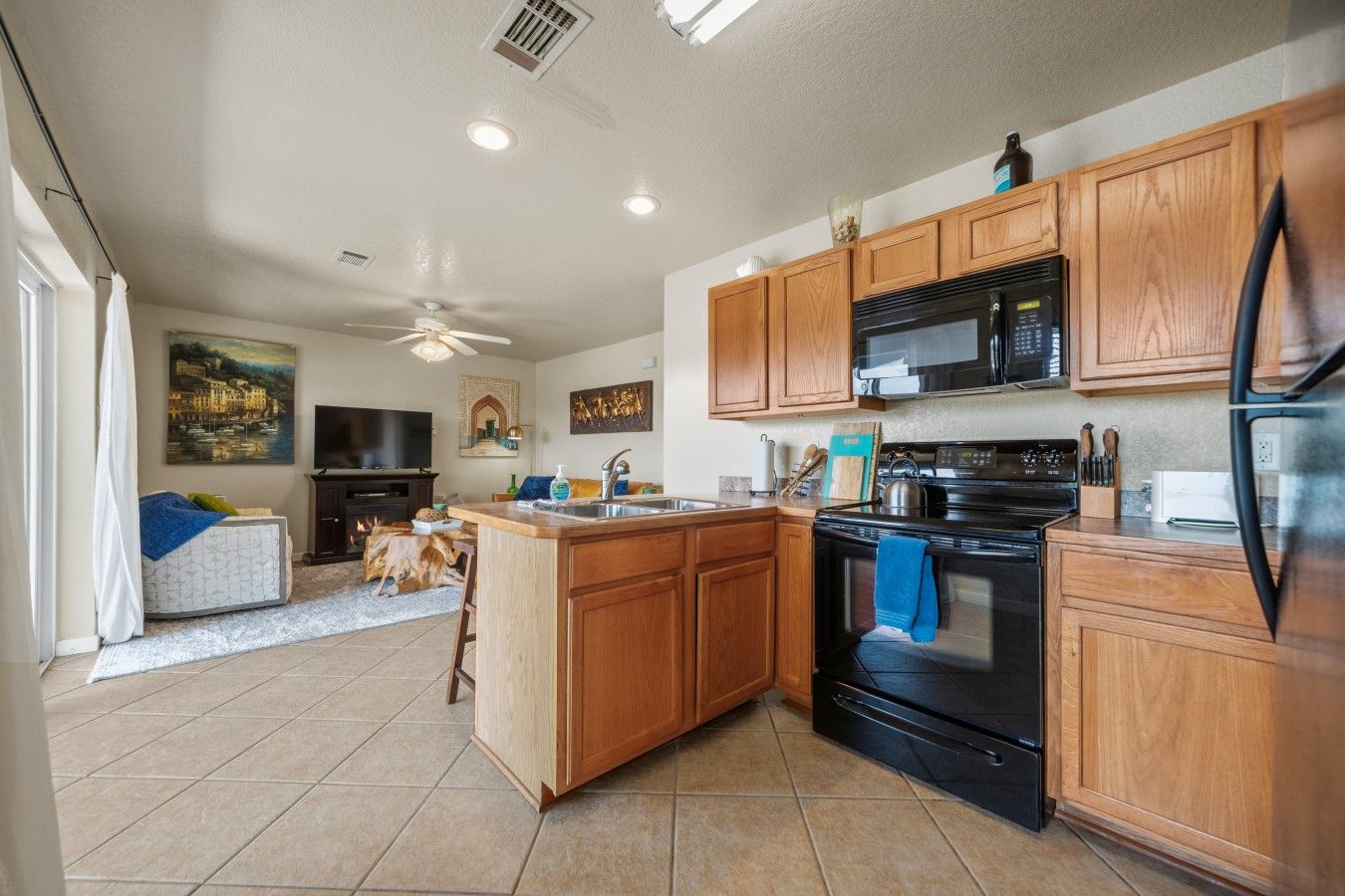 A kitchen with wooden cabinets, a black stove, a microwave, and a refrigerator.