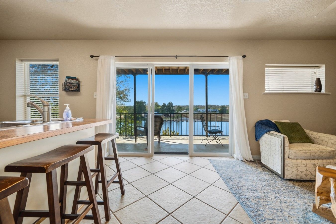 Cozinha com área de bar, mesa de jantar com cadeiras, sofá e vista para um lago através de uma porta de correr de vidro.