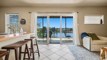 Una cocina con barra, una mesa de comedor con sillas, un sofá y vista a un lago a través de una puerta corrediza de vidrio.