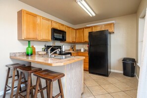 Una cocina con armarios de madera, un refrigerador negro, un microondas, un lavamanos y una zona con taburetes de bar.